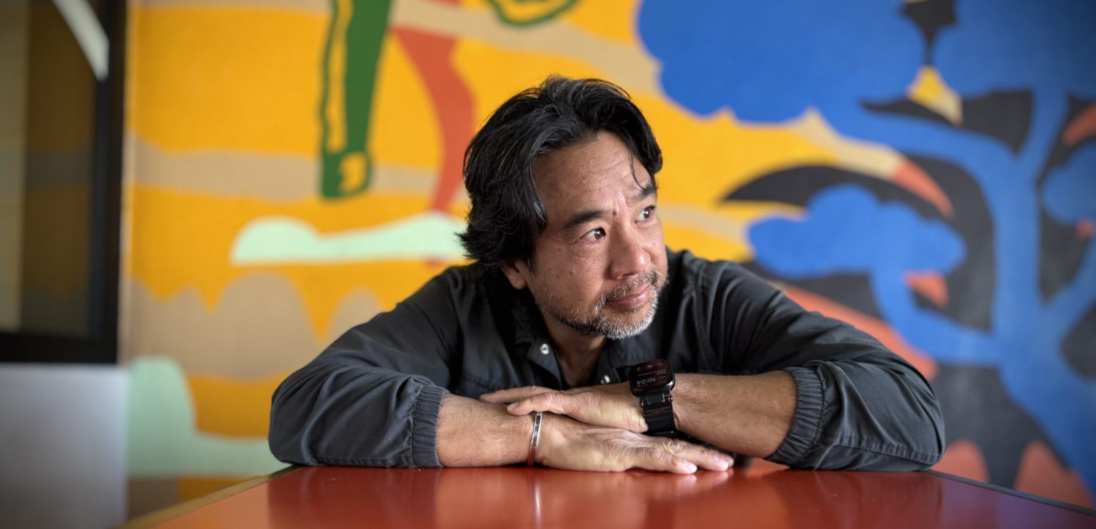 Art Chudabala, author of Back to One, seated in front of a colorful mural