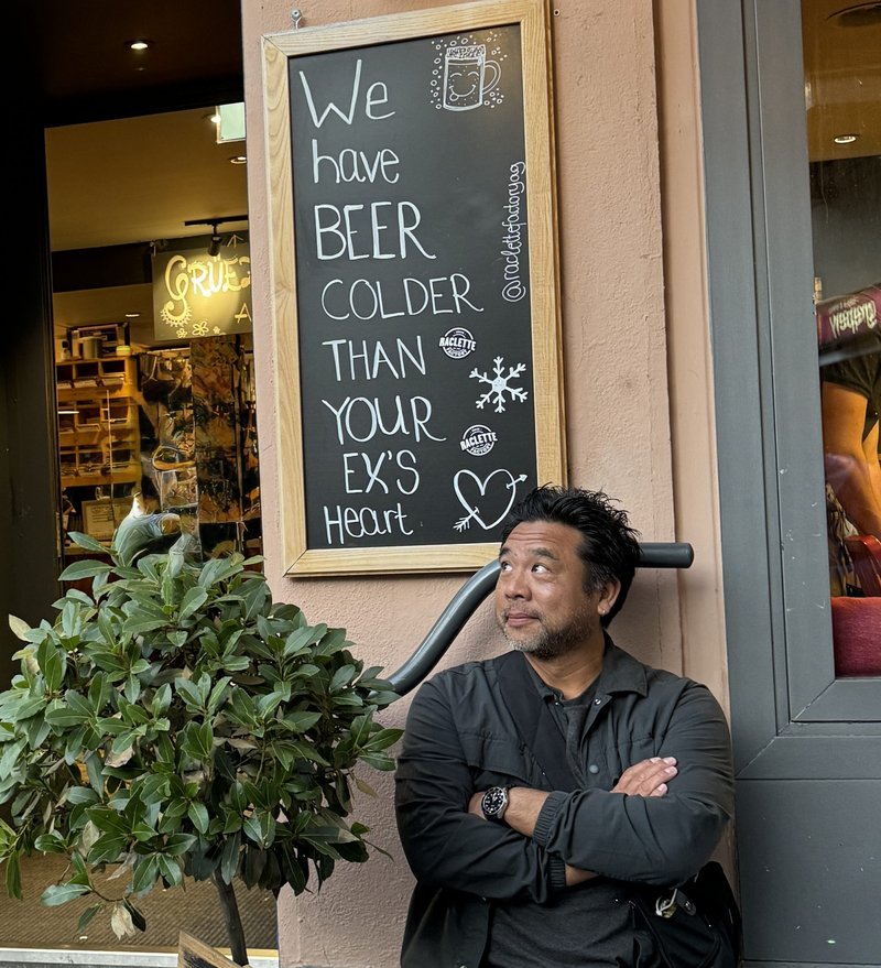 Art Chudabala sitting under a chalkboard sign that reads: We have beer colder than your ex's heart